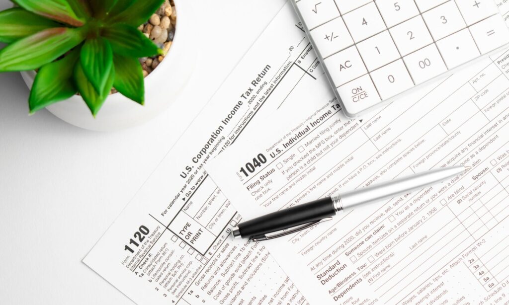 Copies of blank 1120 and 1040 Tax forms on desk with pen
