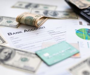 Bank account form, debit card, cash, and financial documents with charts and a calculator on a desk.